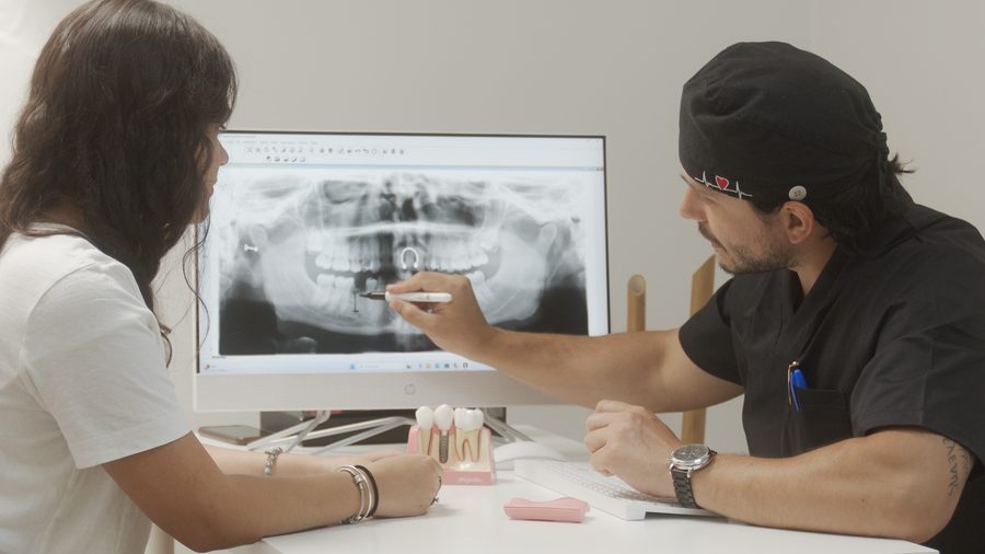 Una paciente revisa su radiograf&iacute;a panor&aacute;mica en pantalla con el doctor, que le se&ntilde;ala la zona del implante